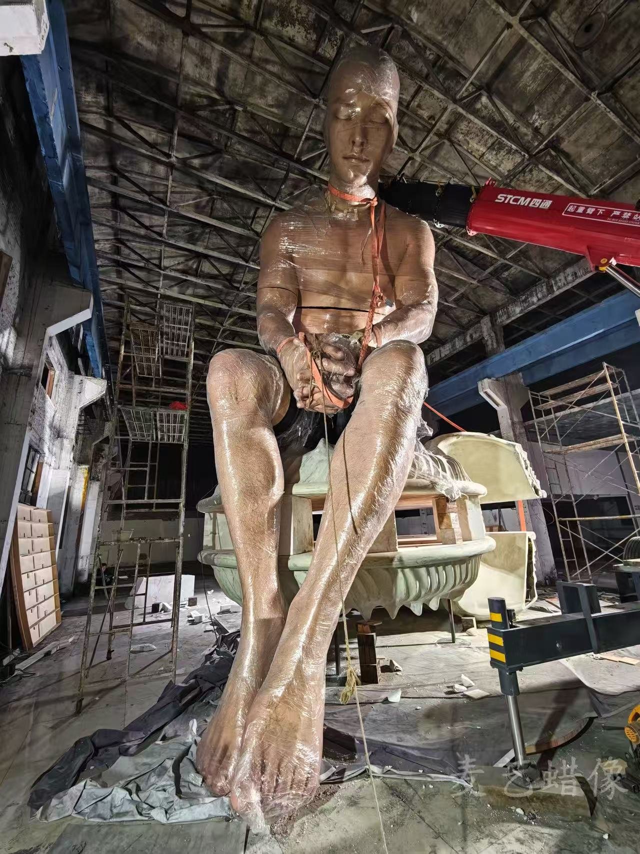Monumental seated portrait sculpture wrapped during assembly in a scaffolded workshop