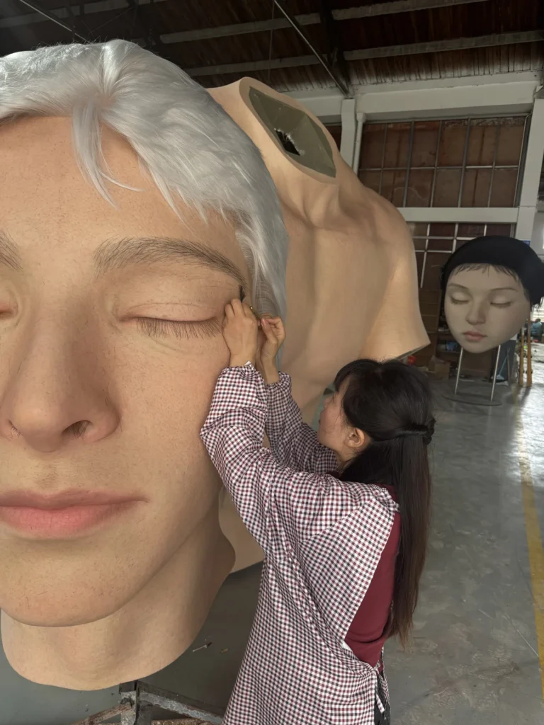 Artist hand-finishing the surface of a giant human face sculpture.