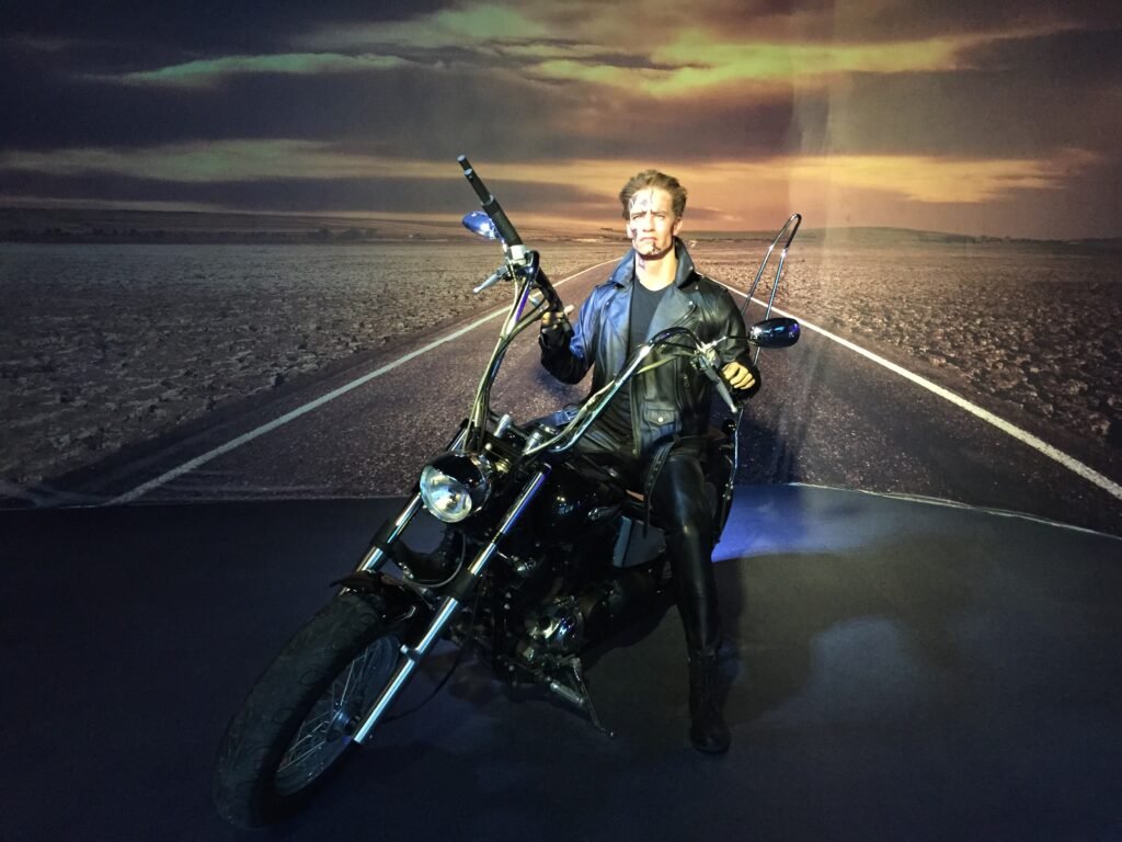 Arnold Schwarzenegger wax figure mounted on a motorcycle in a museum exhibit setting.