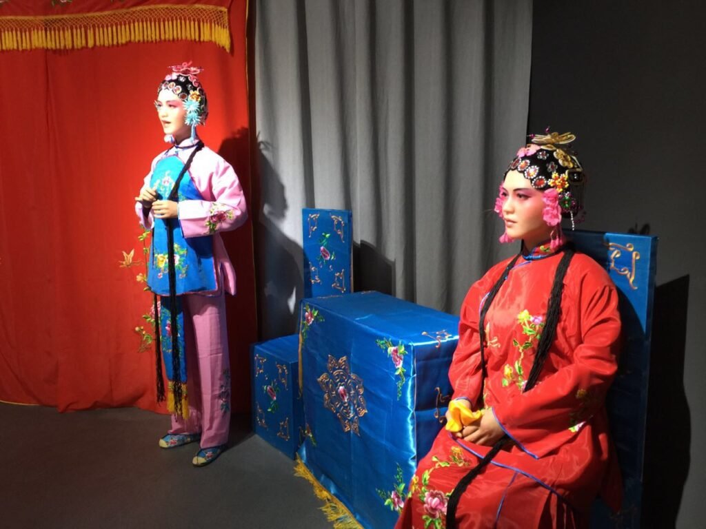 Detailed portrait of Chinese opera female character wax figure showing intricate hair headpiece and pink makeup.