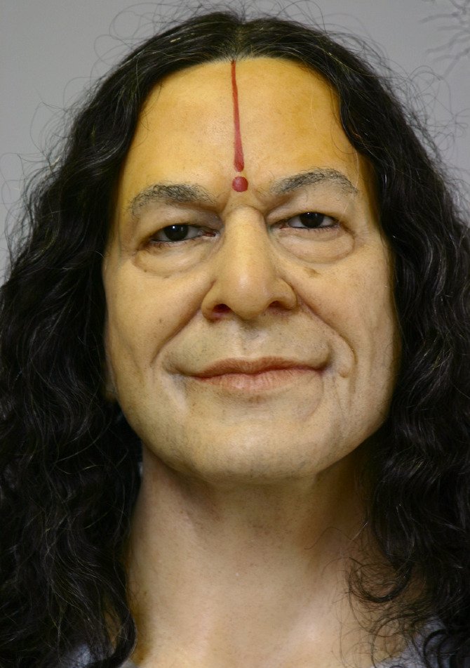 Close-up face detail of Indian spiritual master wax figure with forehead Tilak and smiling expression.