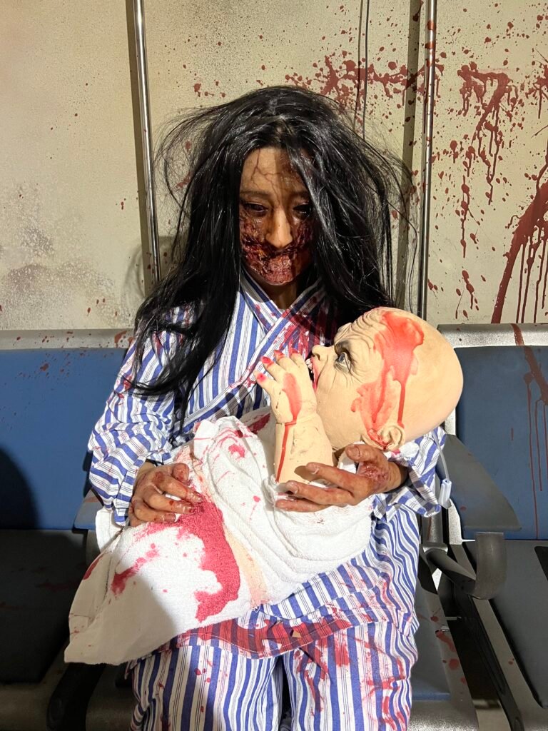 Horror theme attraction wax figure installation set in an abandoned hospital environment.